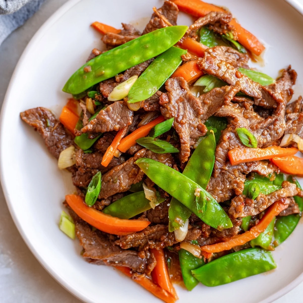 A close-up of beef stir-fry with snow peas, carrots, and ginger served over steamed rice.