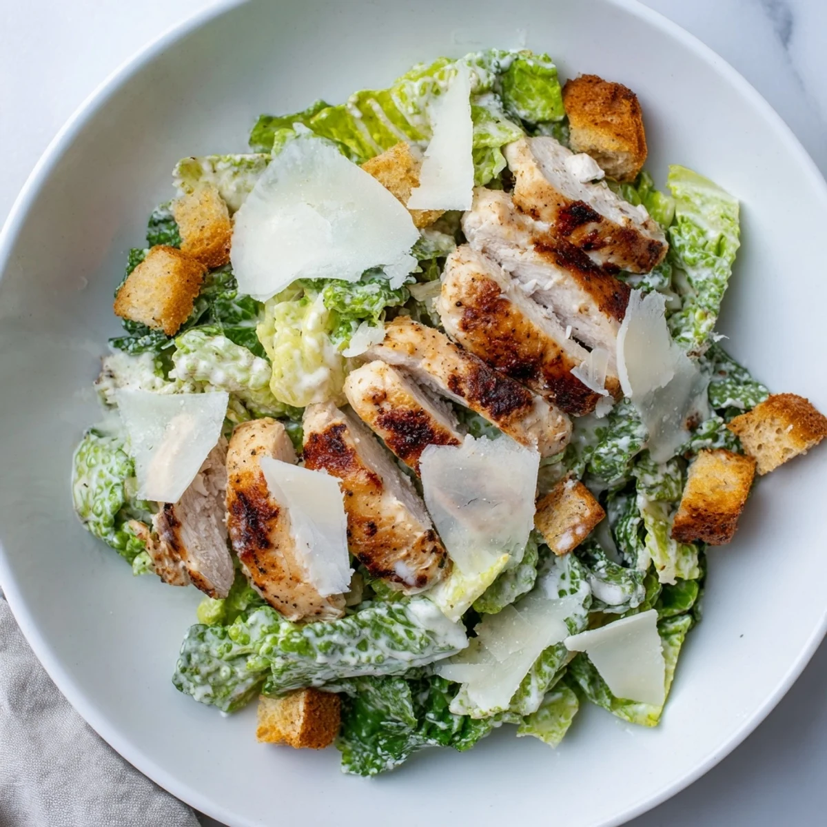 Served in a rustic wooden bowl, this Chicken Caesar Salad features chopped romaine, savory garlic croutons, and sliced grilled chicken drizzled with creamy dressing.
