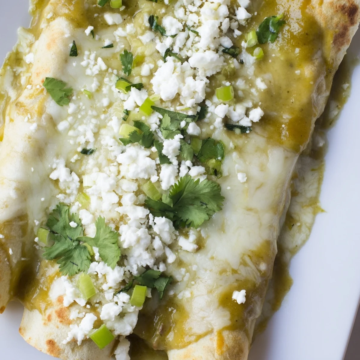 A close-up of Beef Enchiladas with Green Sauce reveals layers of savory beef, melted Monterey Jack, and a creamy, mildly spicy sauce.
