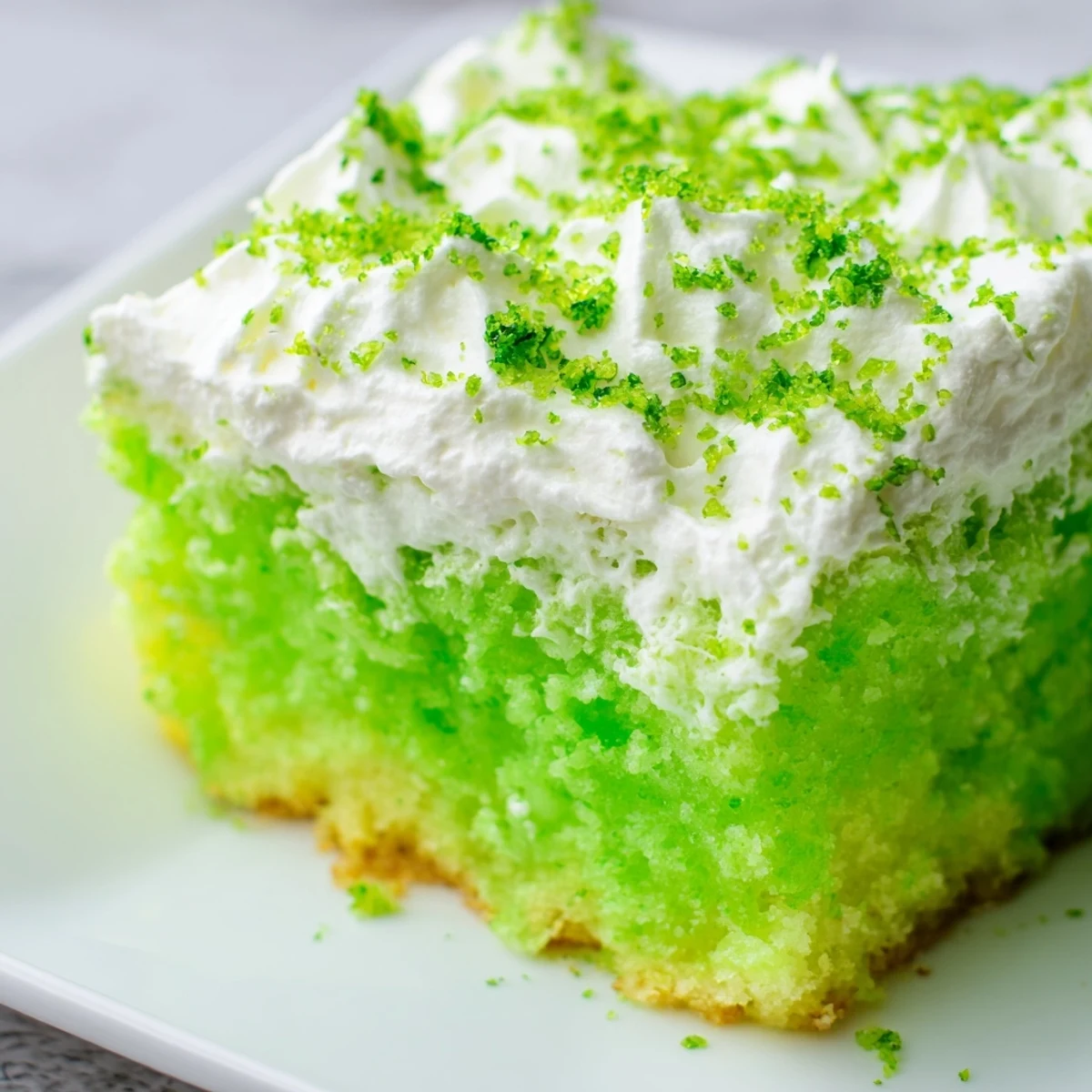 St. Patrick's Day Lime Poke Cake garnished with lime zest, served on a festive green plate perfect for celebrations.