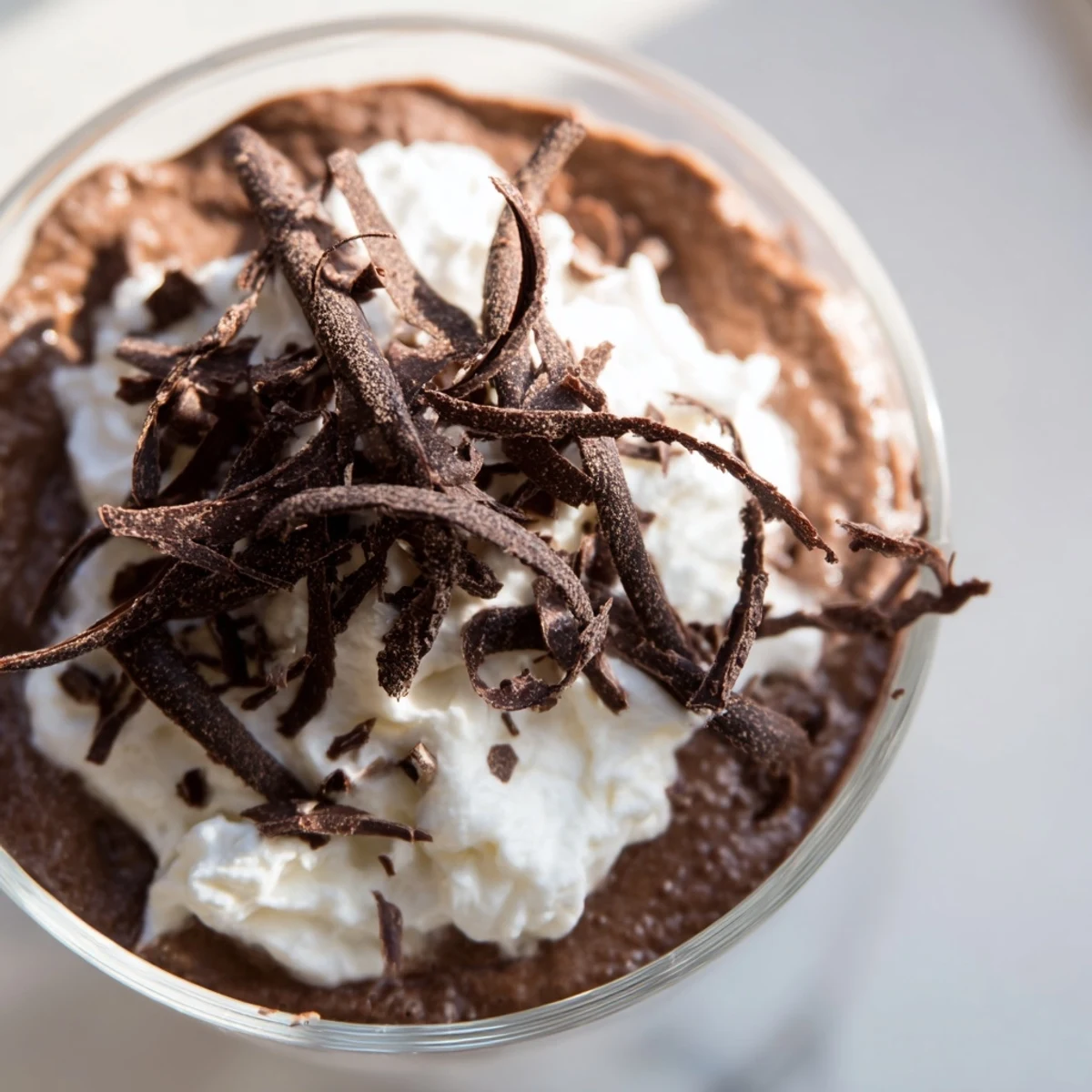 Four small glass dessert cups filled with rich chocolate mousse, each topped with a generous swirl of light whipped cream and delicate dark chocolate curls, served chilled.