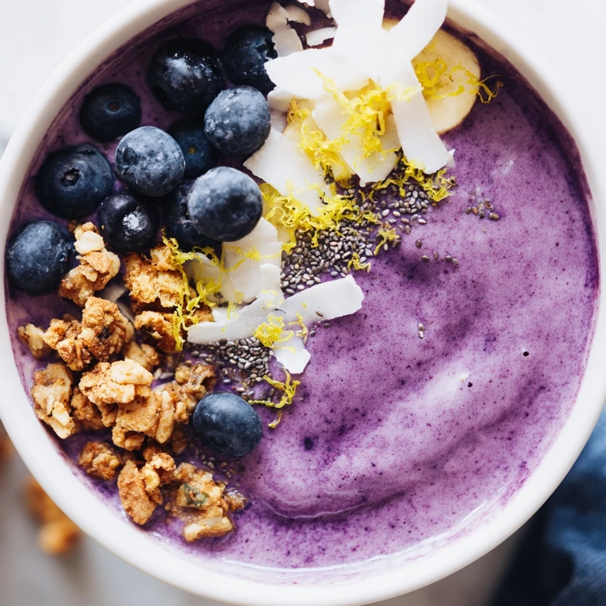 Close-up of a thick Lemon Blueberry Smoothie Bowl with coconut flakes and lemon zest garnish on top.  