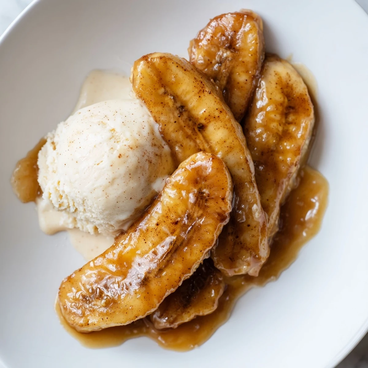 Caramelized bananas Foster in a rich brown sugar sauce, spooned over a scoop of creamy vanilla ice cream.