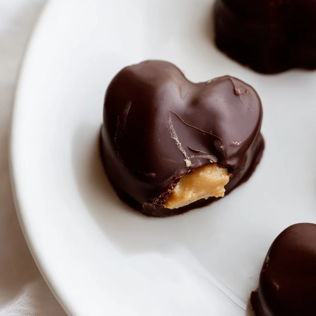Homemade chocolate peanut butter hearts with a smooth, glossy dark chocolate coating on a marble slab.