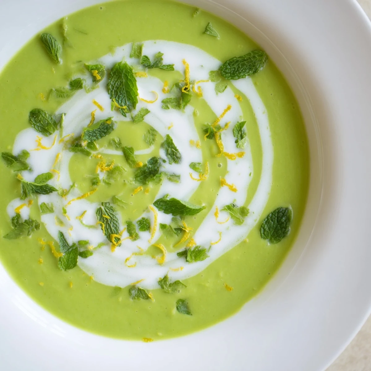 Ladle of Spring Pea Soup with Mint and Crème Fraîche being poured into a white ceramic bowl, revealing its velvety, smooth texture.