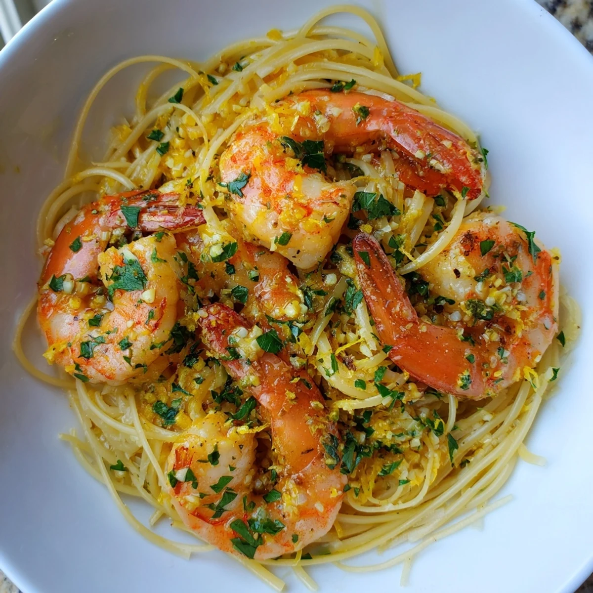 A close-up shows succulent shrimp tangled in delicate angel hair pasta, drenched in a bright, aromatic lemon garlic butter sauce.