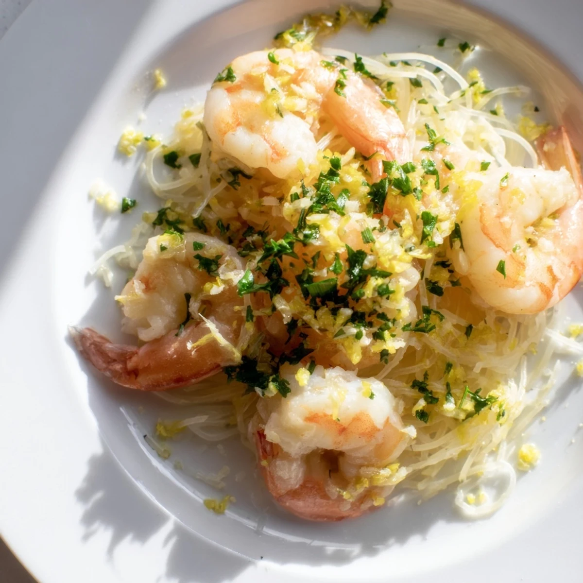 A close-up of Lemon Garlic Butter Shrimp with Angel Hair Pasta glistening with lemon wedges and fresh parsley on a white plate.