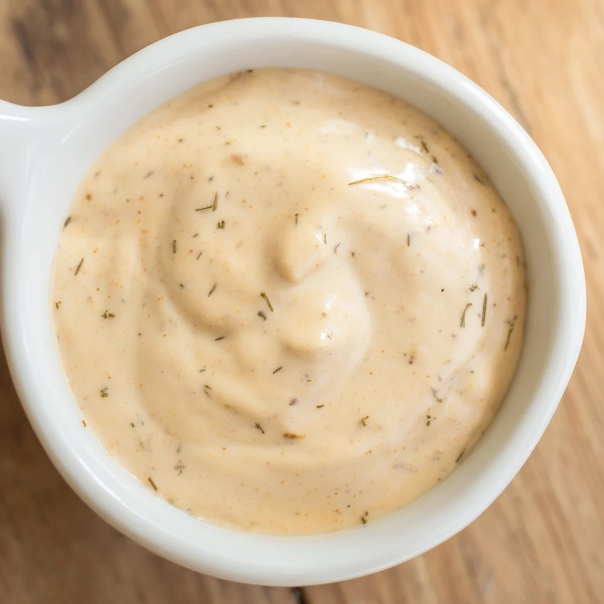 A glass jar of hot honey ranch crispy chicken tenders sauce sits on a wooden board next to crispy tenders and a napkin.