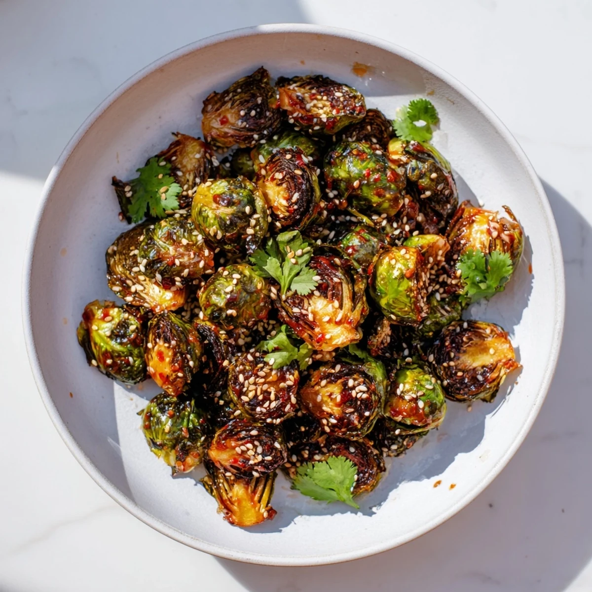 Tender Honey Sriracha Brussels Sprouts tossed in a glossy sauce and topped with fresh cilantro for serving.