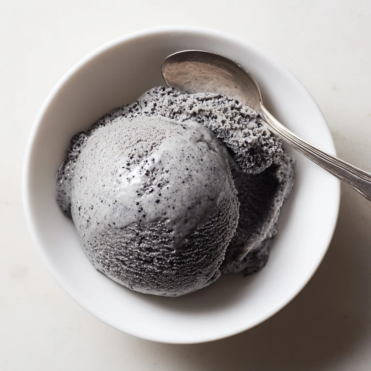 Creamy Toasted Black Sesame Ice Cream scooped in a bowl, topped with sesame seeds and a honey drizzle for dessert.