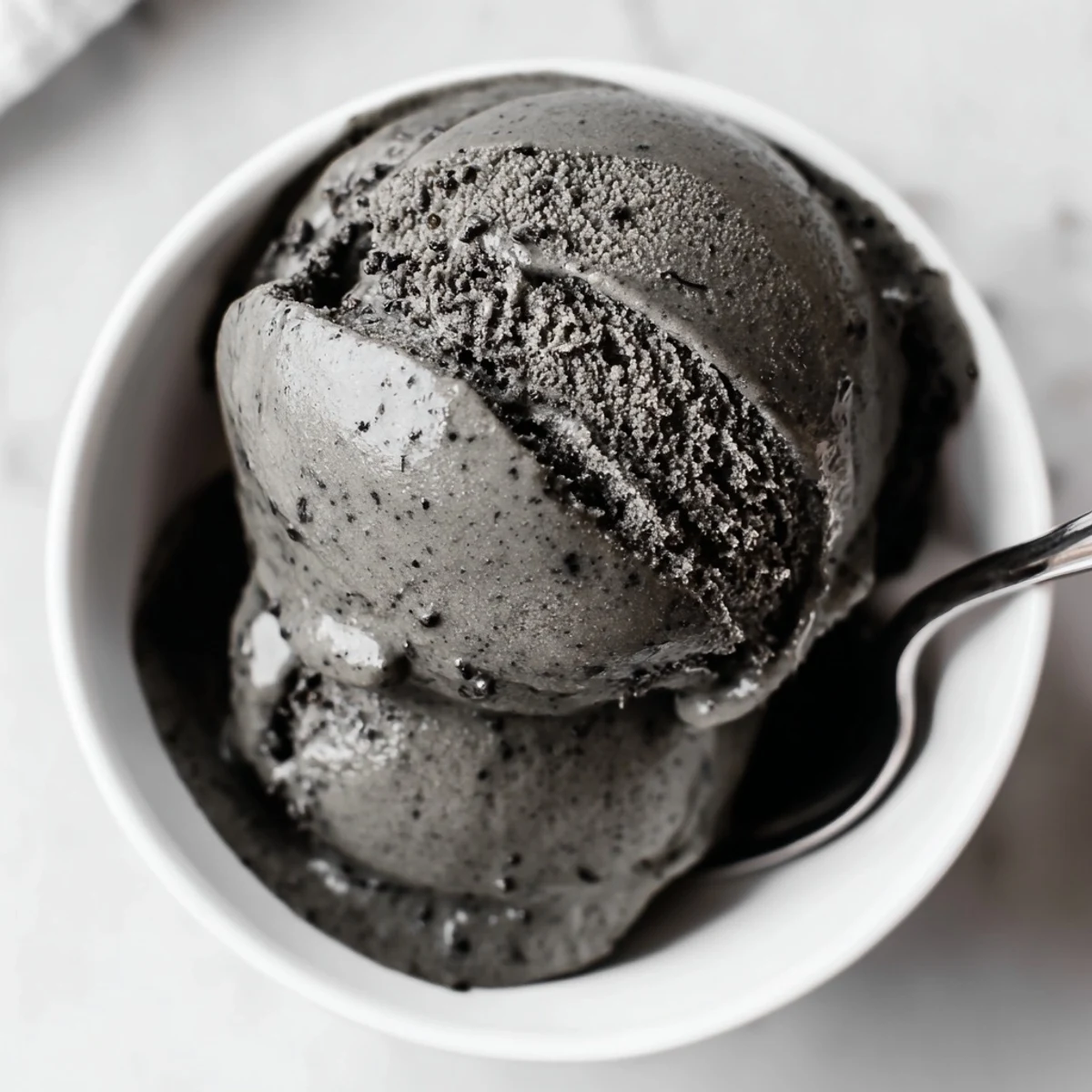 Scoop of Toasted Black Sesame Ice Cream melting slightly on a chilled plate, garnished with toasted seeds for texture.