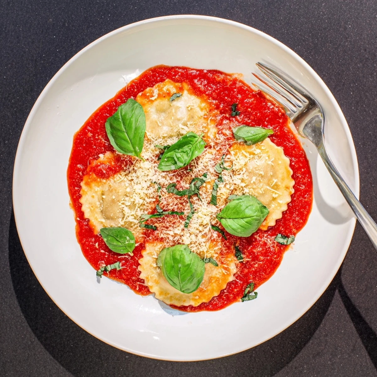 A close-up of 20-Minute Ravioli with Simple Sauce steaming on a white plate, garnished with fresh basil and grated Parmesan.