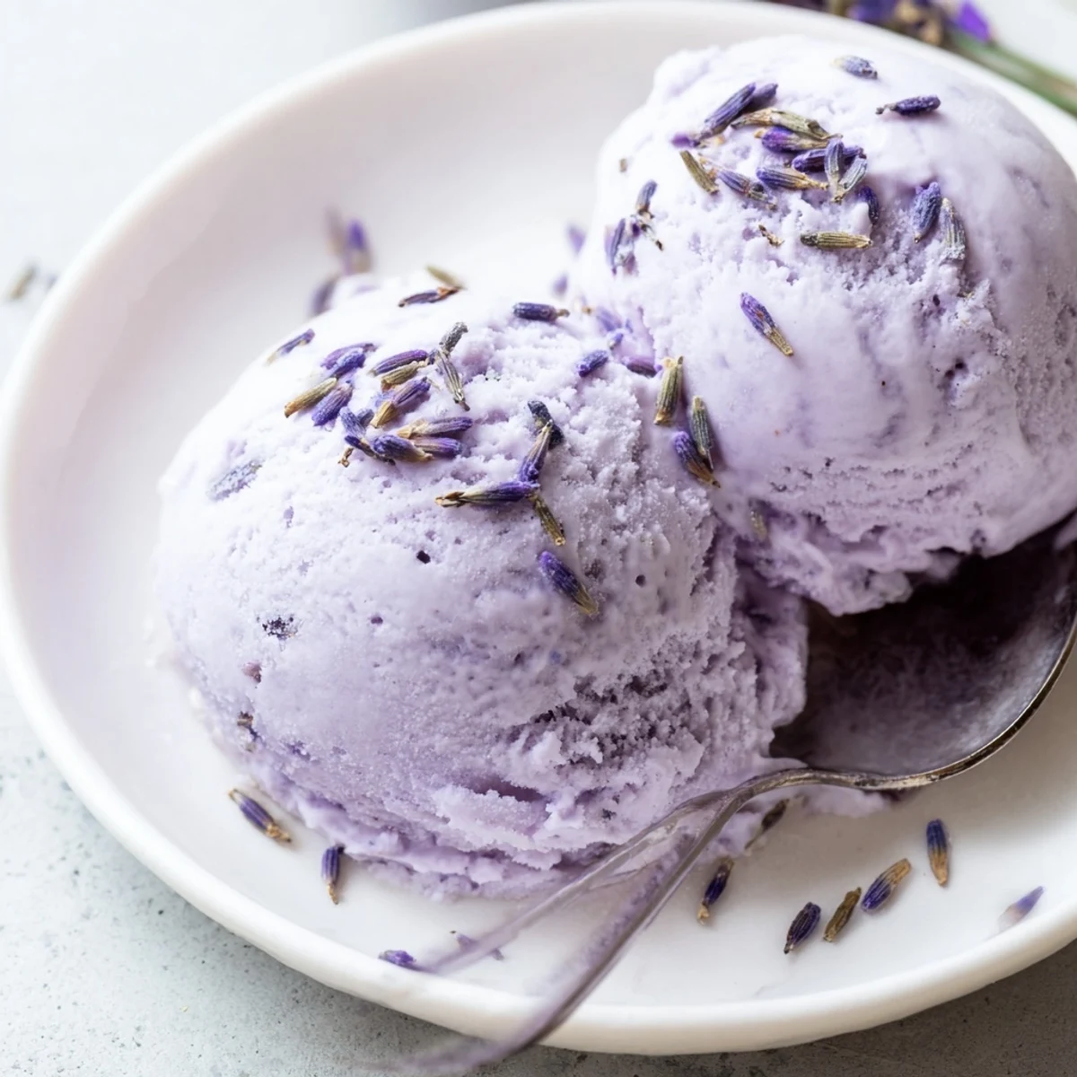 Scoops of creamy Lavender Ice Cream sit in a glass dish with a backdrop of fresh berries and shortbread cookies.