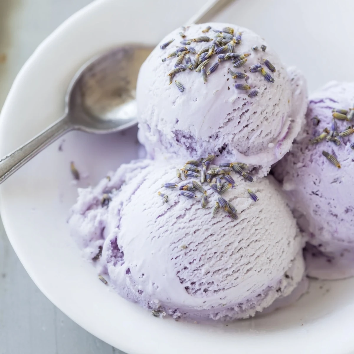 A bowl of homemade Lavender Ice Cream is ready to serve on a sunny patio table beside iced tea.