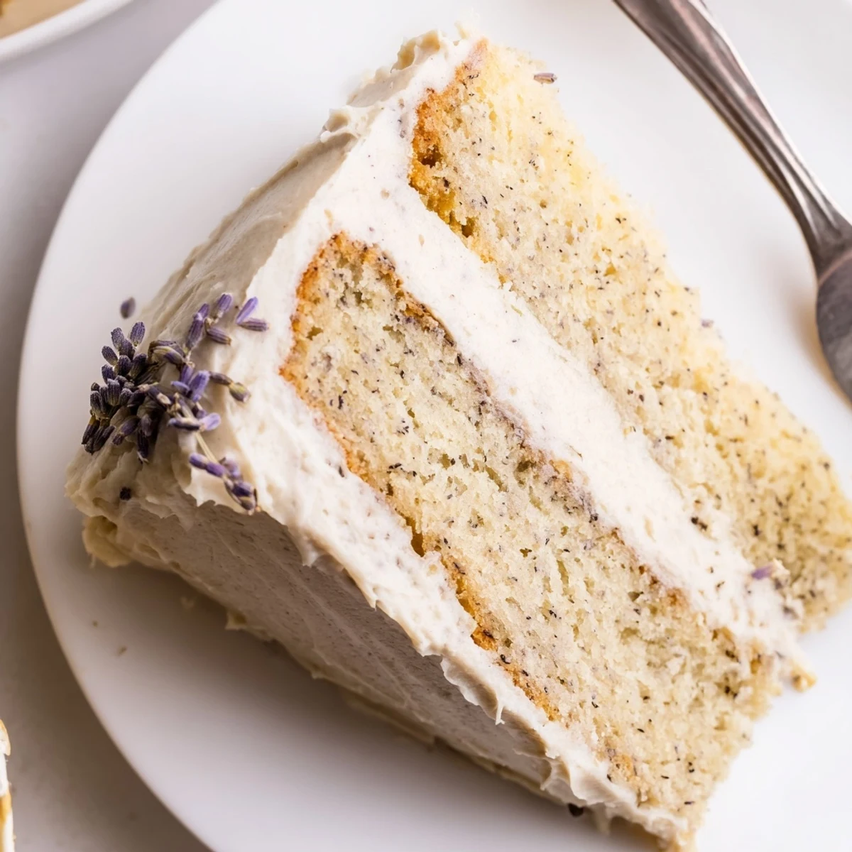 Two-layer Earl Grey lavender cake topped with vanilla frosting and dried buds, cut for generous party slices.
