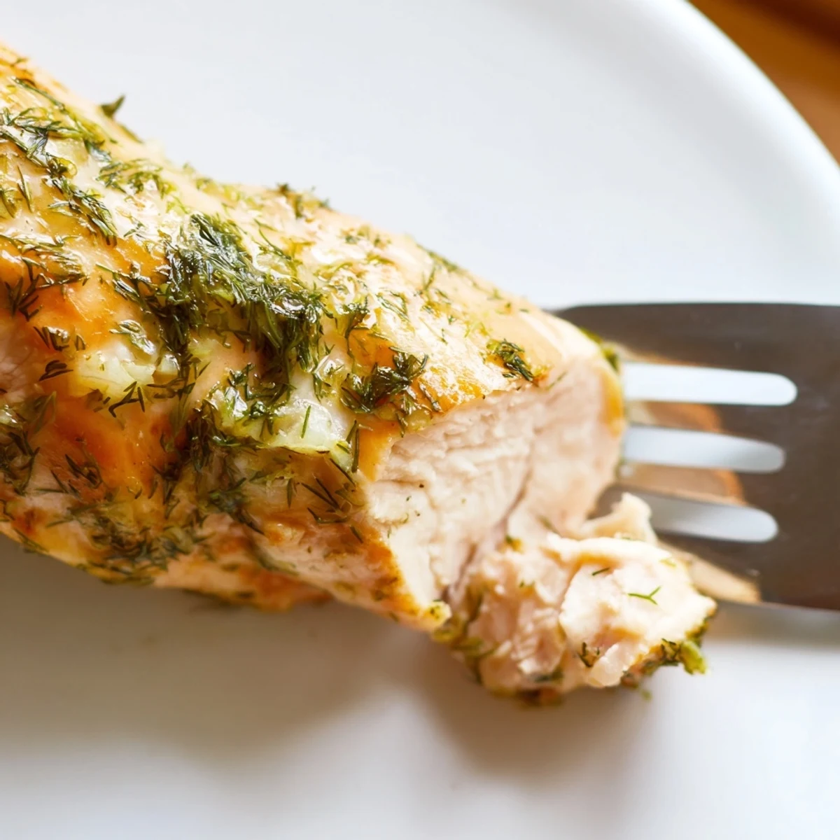 Freshly baked Paleo Lemon Dill Chicken rests on a white plate, garnished with bright lemon slices and chopped herbs.