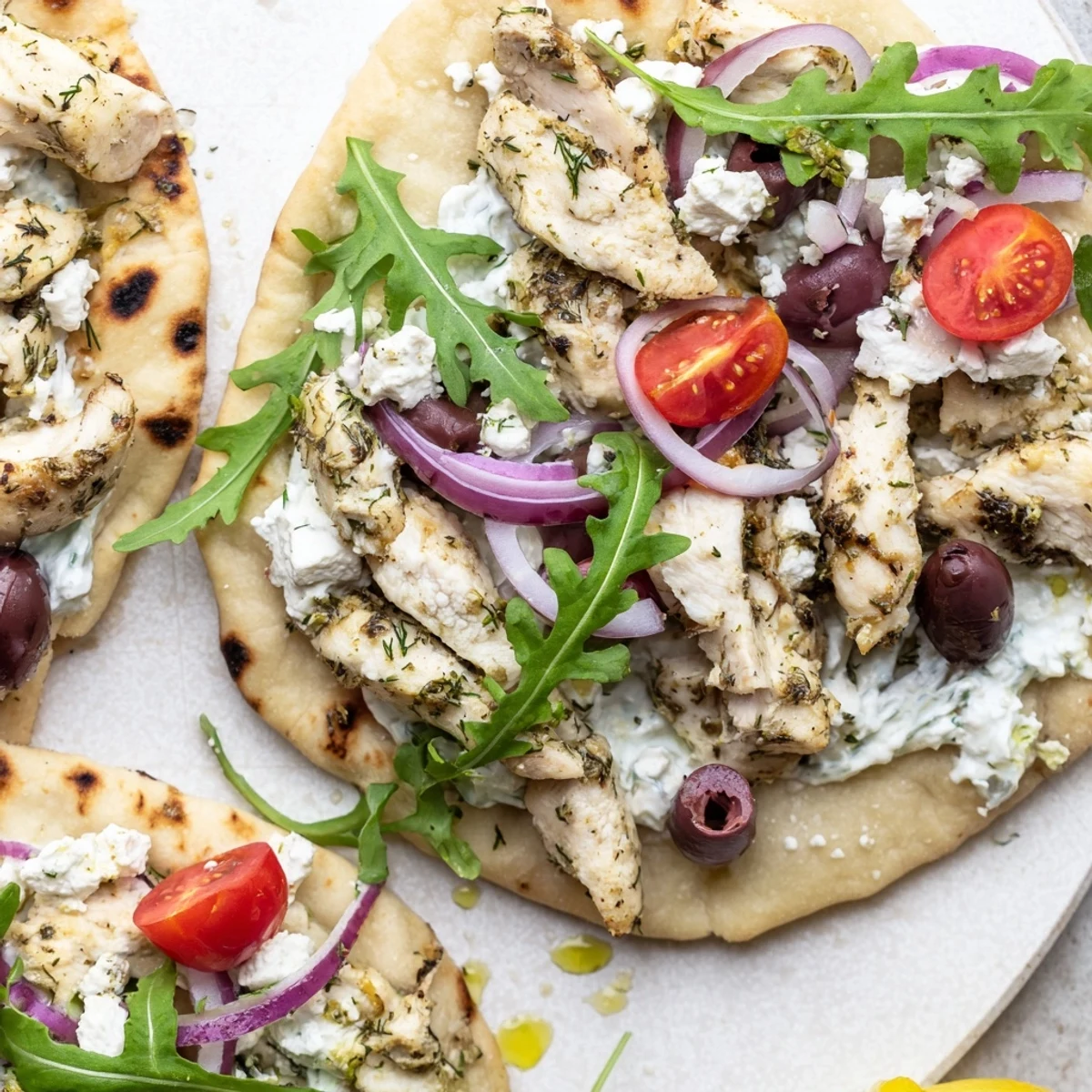 Sliced lemon herb chicken on warm flatbread topped with creamy feta and fresh arugula.