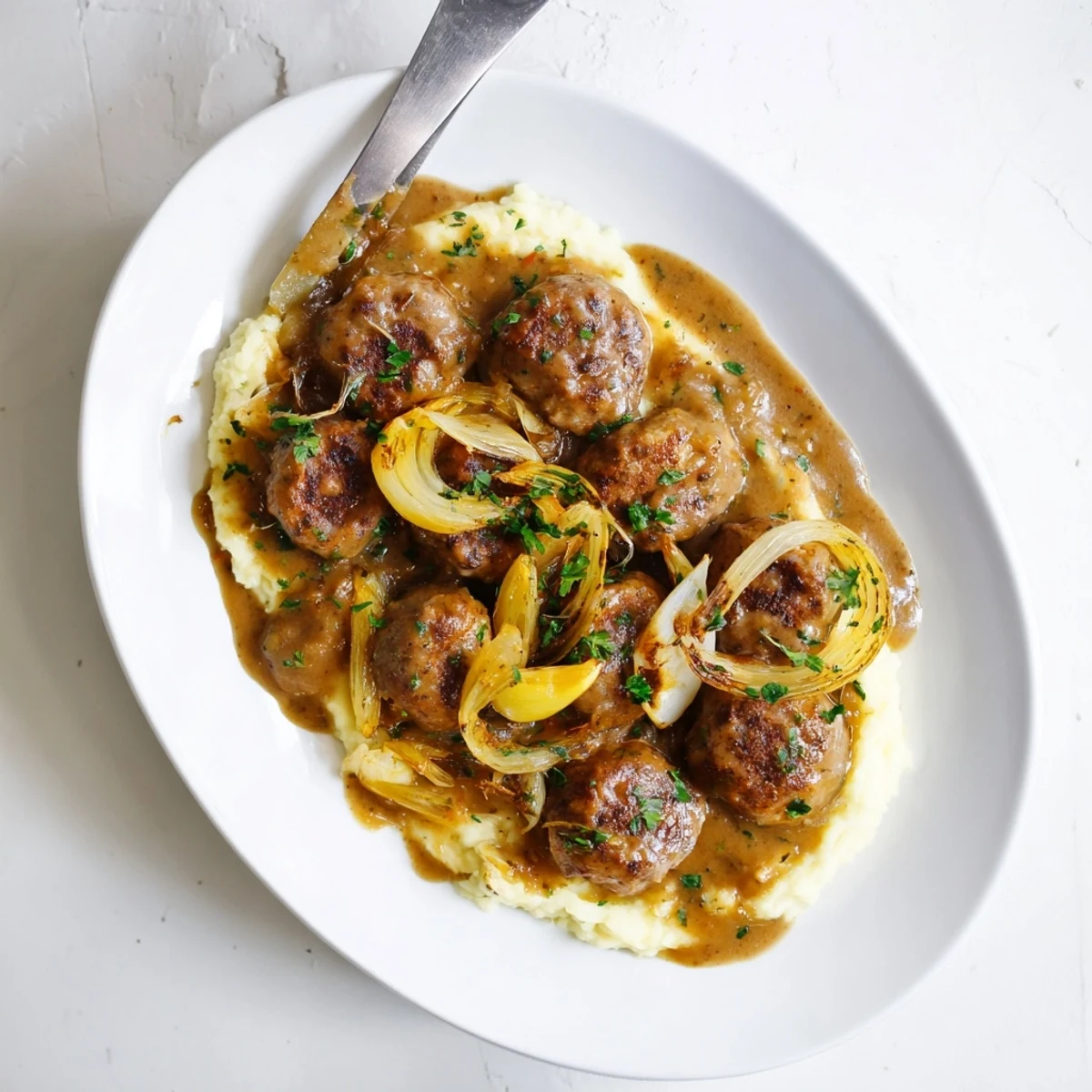 Golden brown Sausages in Onion Gravy plated on a white dish, with creamy mashed potatoes and a sprinkle of fresh herbs.