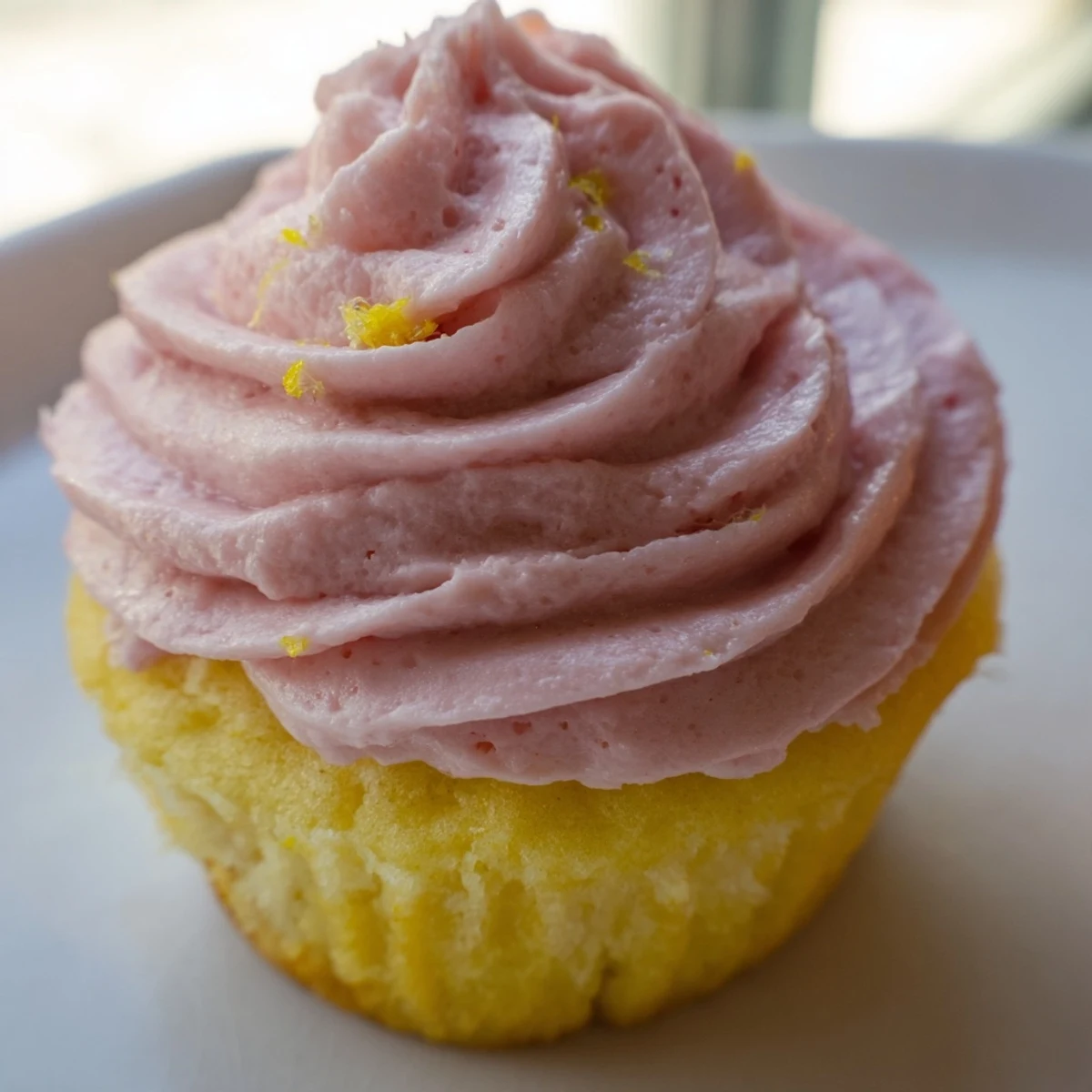 Freshly baked lemon cupcakes with vibrant strawberry buttercream swirled high atop tender yellow crumb.