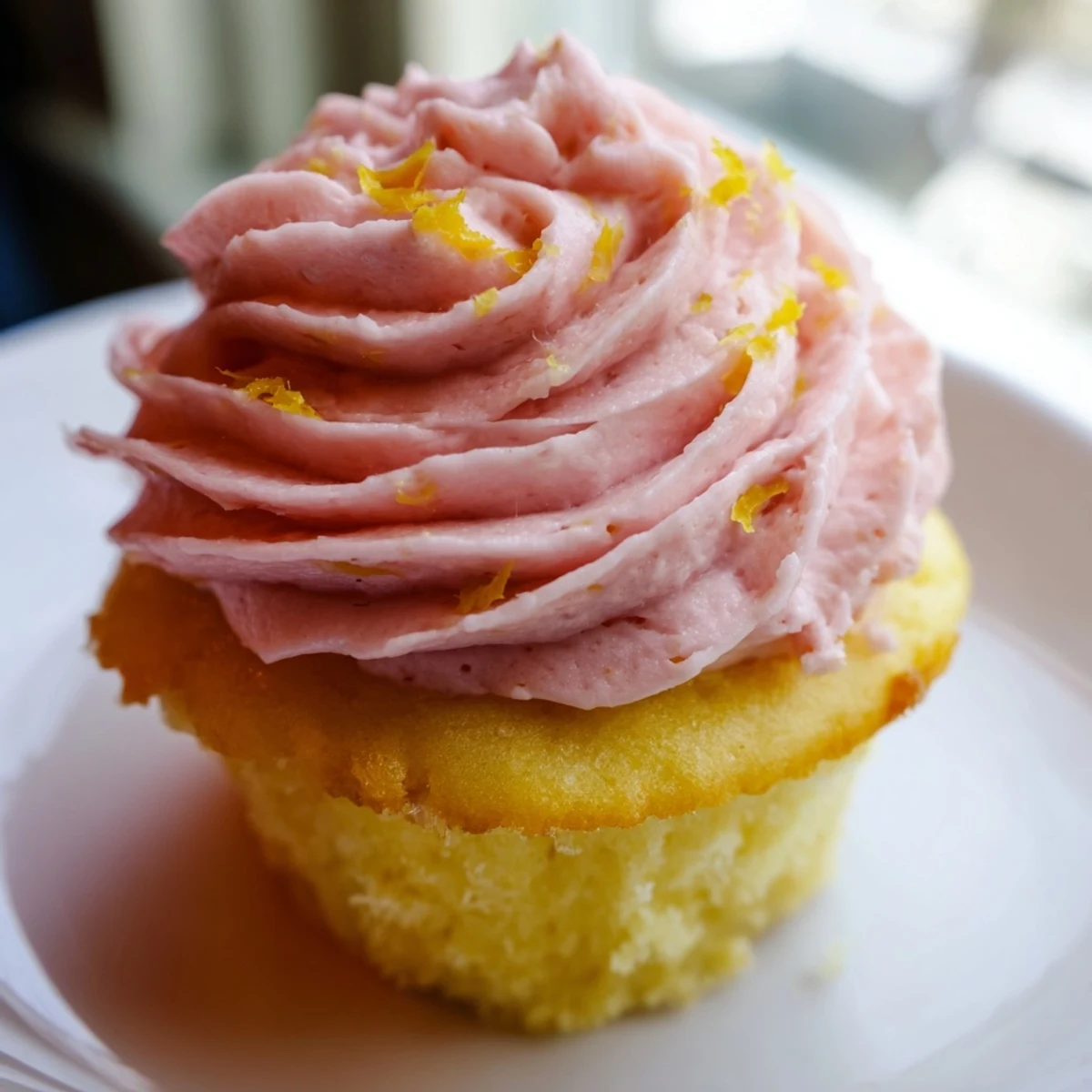 Golden lemon cupcakes topped with swirls of naturally pink strawberry buttercream frosting on a white plate.