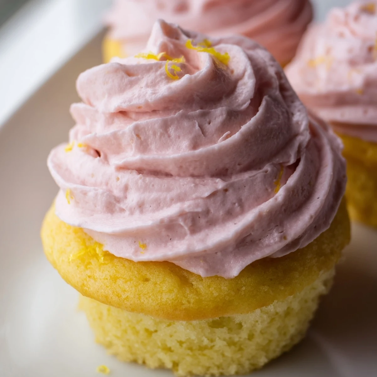 Zesty lemon cupcakes with fluffy pink strawberry buttercream garnished with fresh strawberry slices.