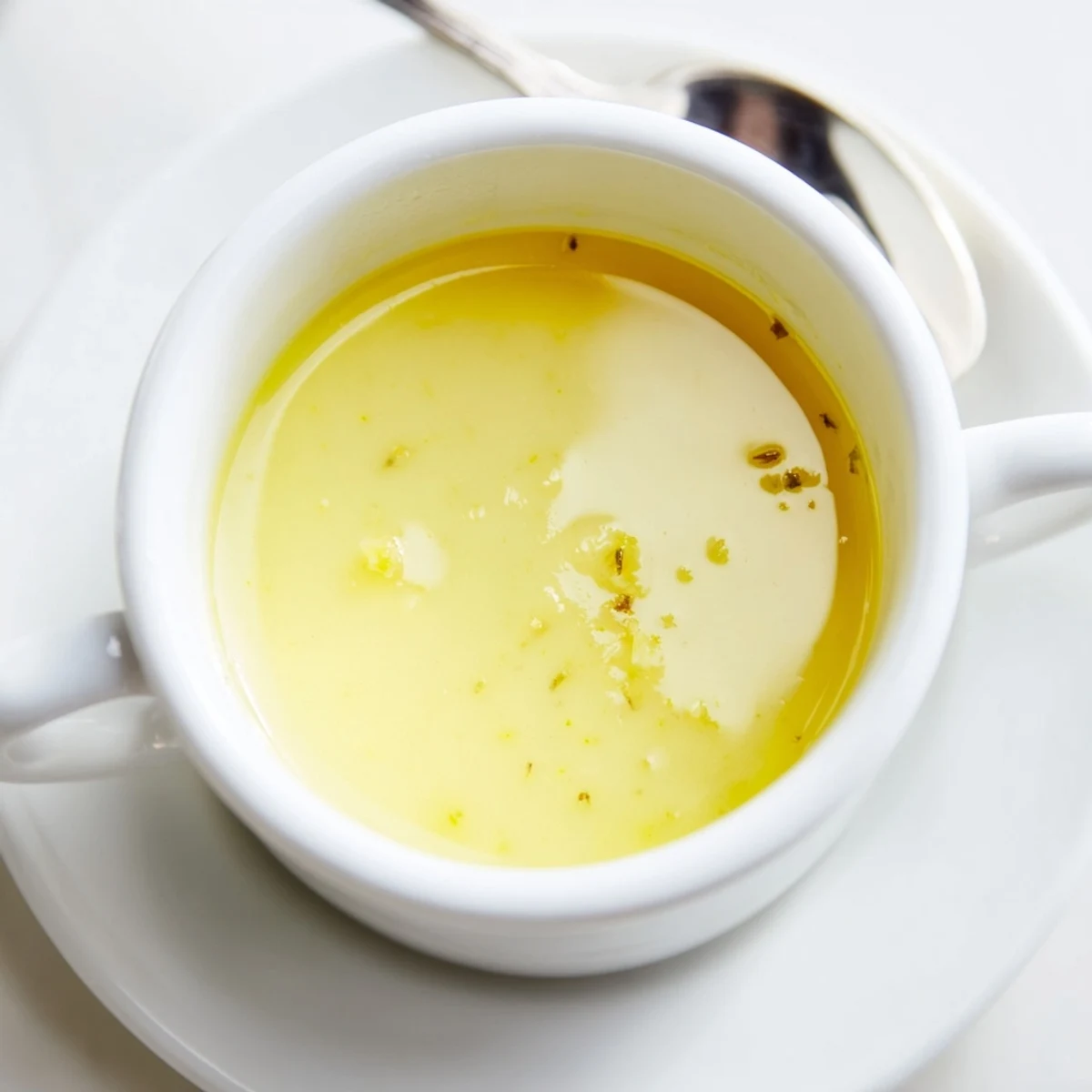 Thick golden yellow lemon vinaigrette dressing whisked in white bowl with olive oil pour