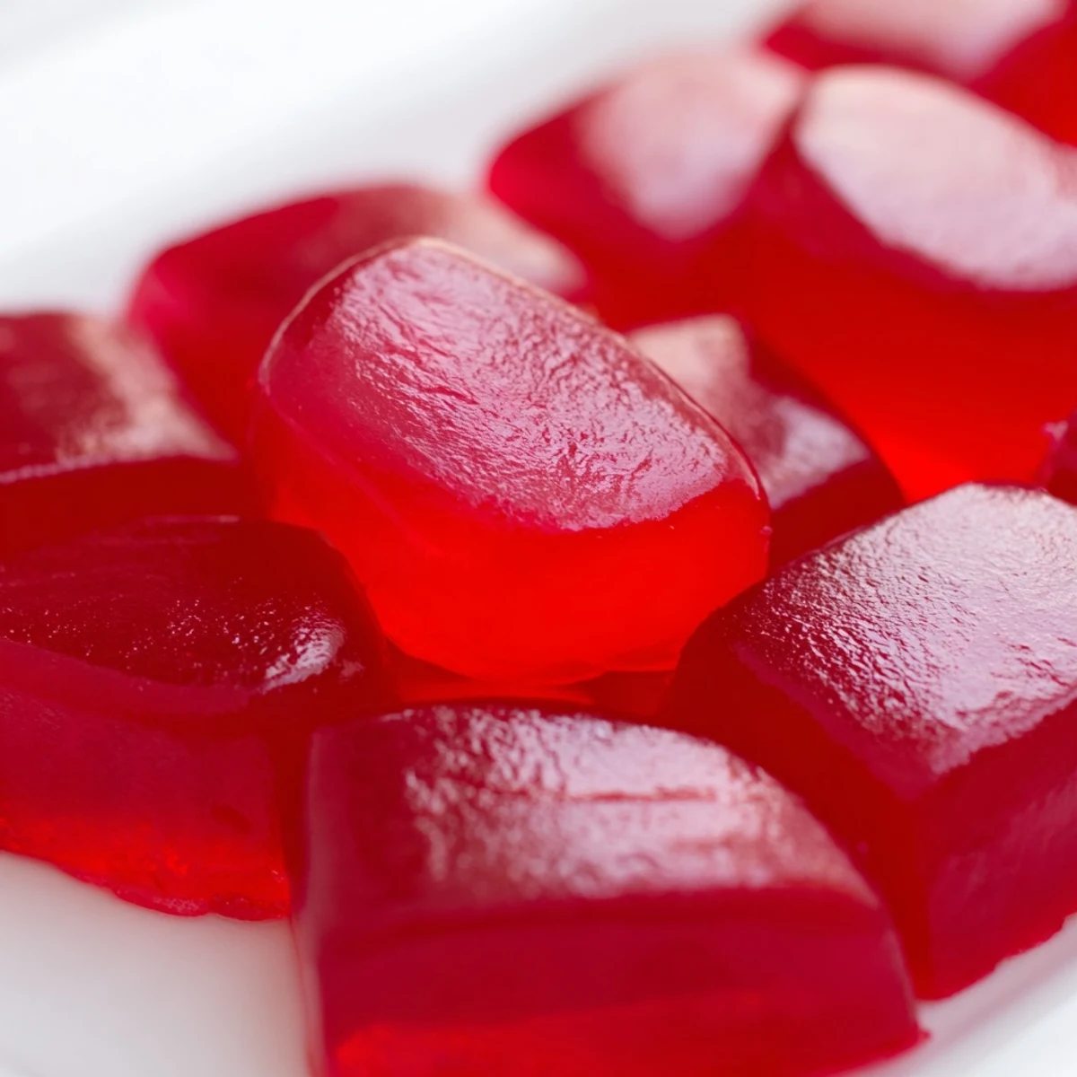 Chewy homemade strawberry gummies arranged on a white plate, showcasing their vibrant red color and glossy finish
