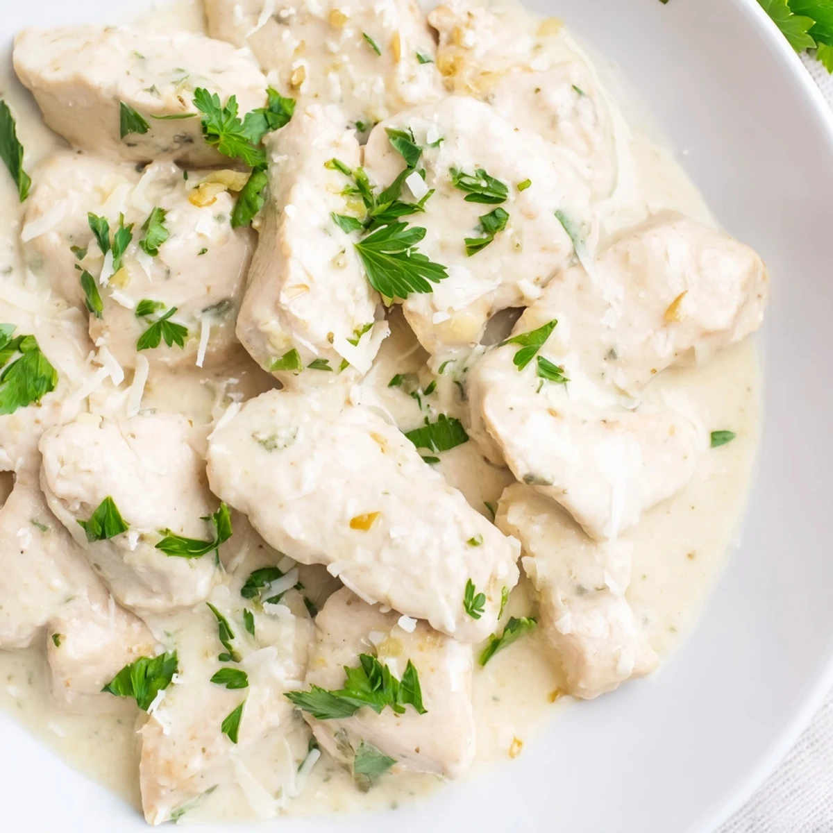 Slow cooker creamy garlic Parmesan chicken served over mashed potatoes with velvety white sauce drizzled on top
