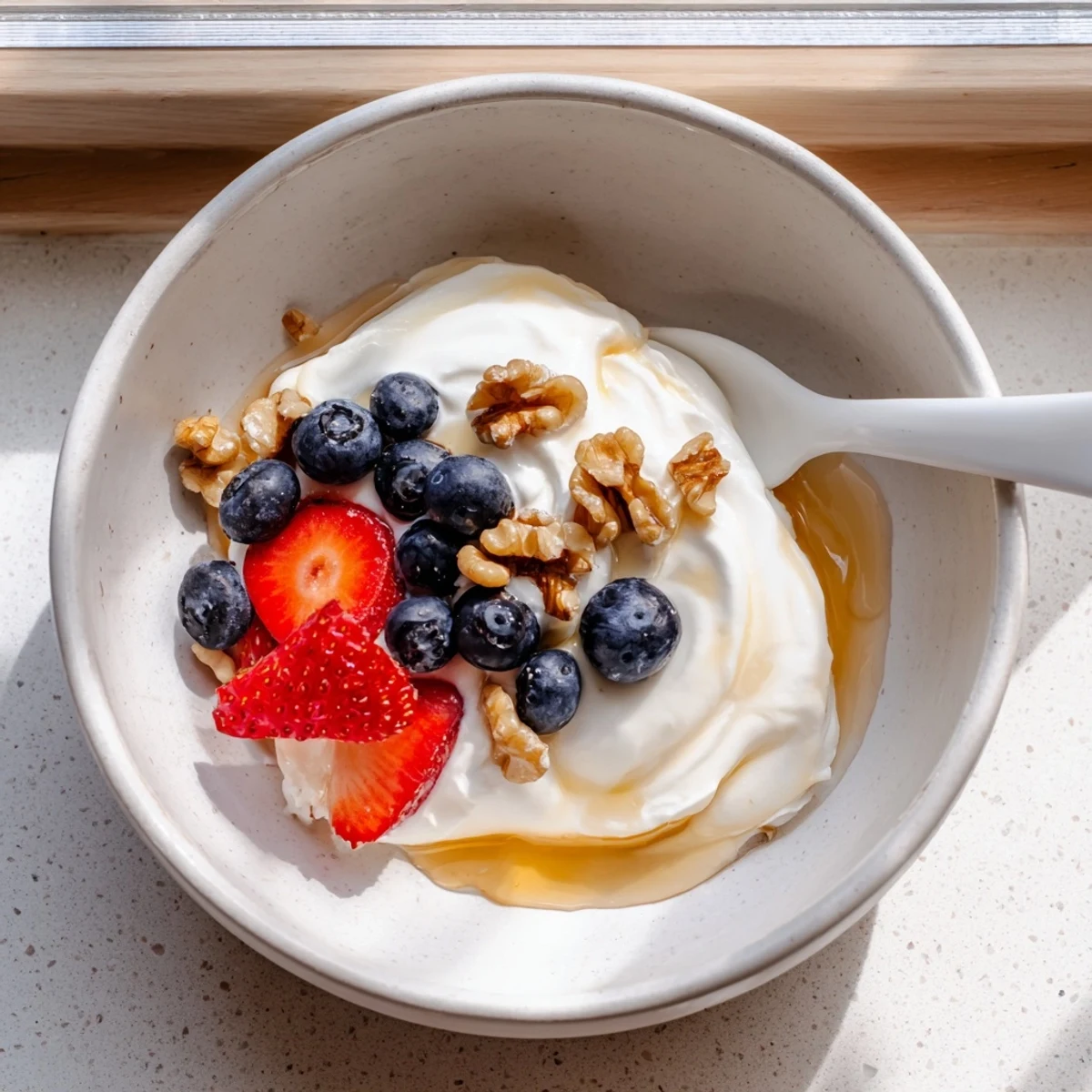 Creamy homemade Greek yogurt in a white bowl topped with fresh honey and walnuts