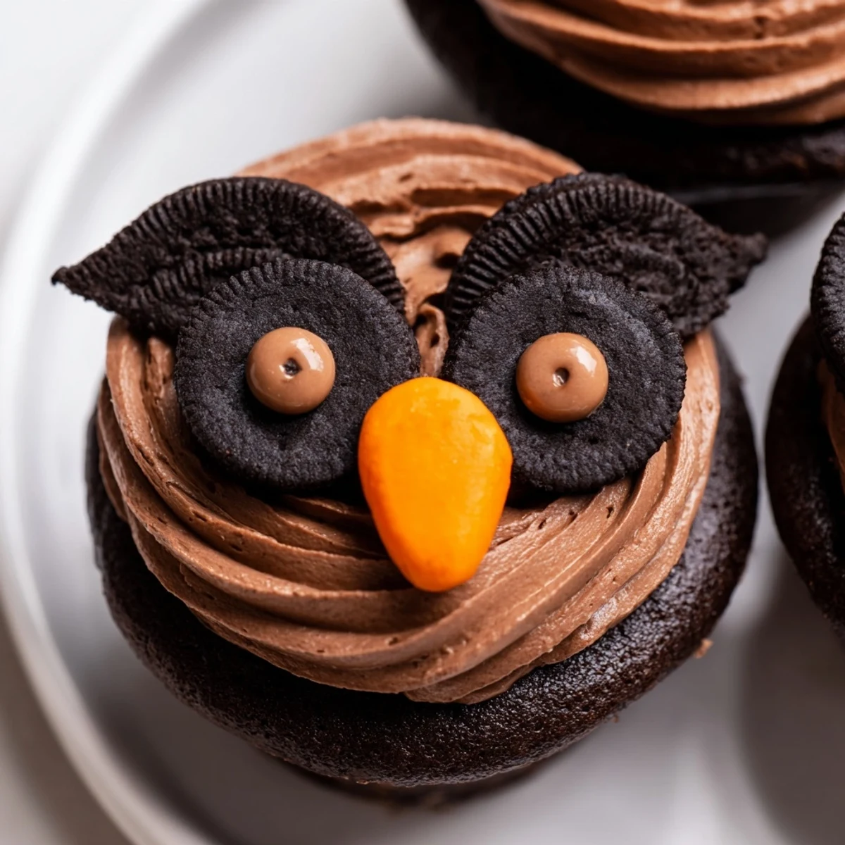 Cute Oreo Owl Cupcakes topped with chocolate frosting and candy eyes on a rustic baking sheet