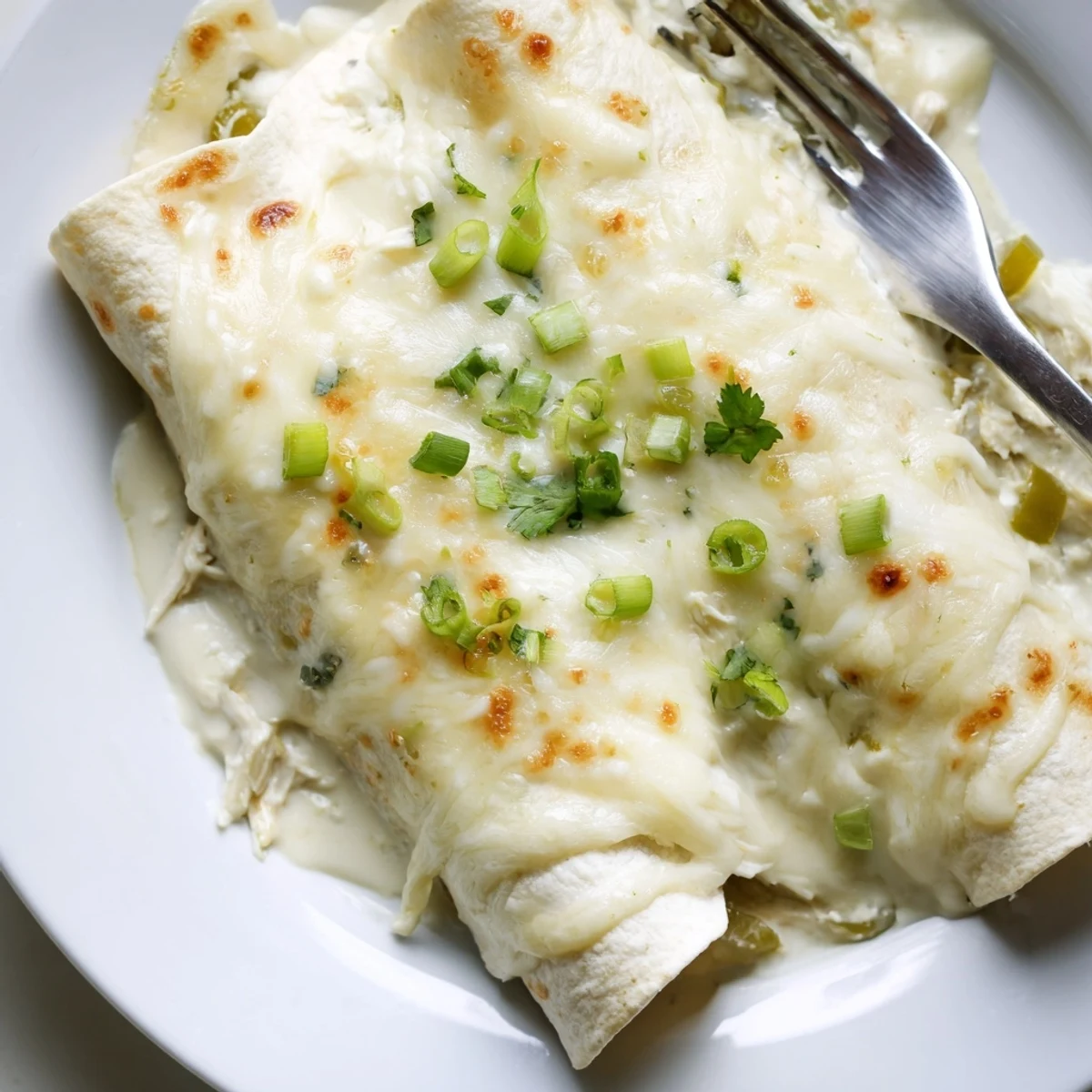 Creamy White Chicken Enchiladas bubbling golden, topped with cilantro and green onions.