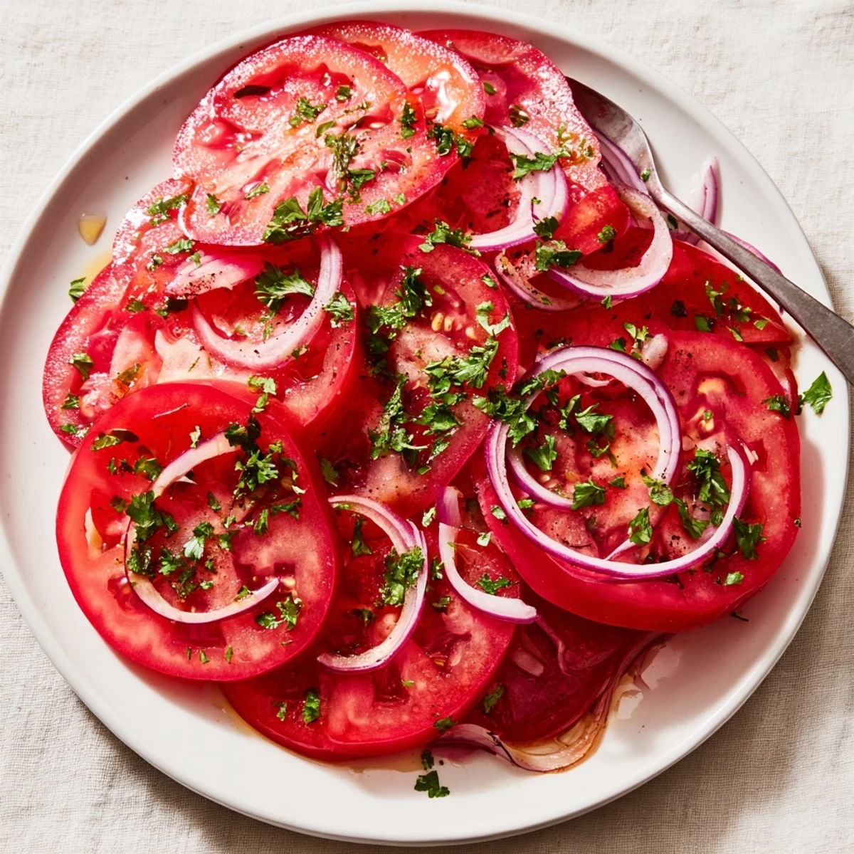 Fresh tomato and onion salad with sliced tomatoes, red onion rings, and parsley drizzled with olive oil vinaigrette on a white serving plate