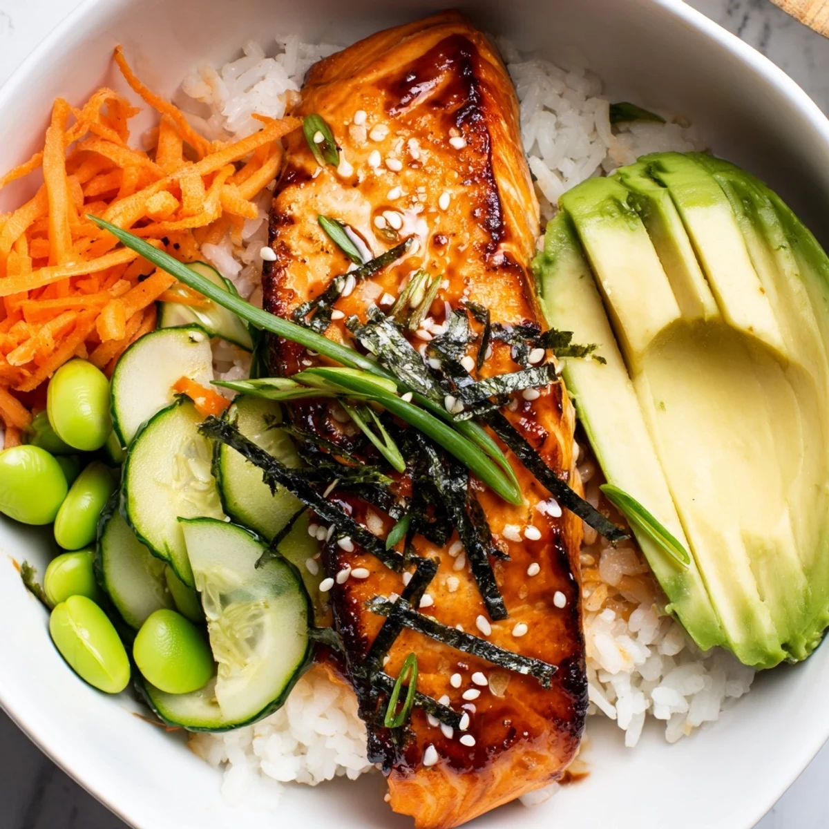 Vibrant salmon and rice bowl topped with colorful julienned carrots, edamame, scallions, and toasted sesame seed garnish