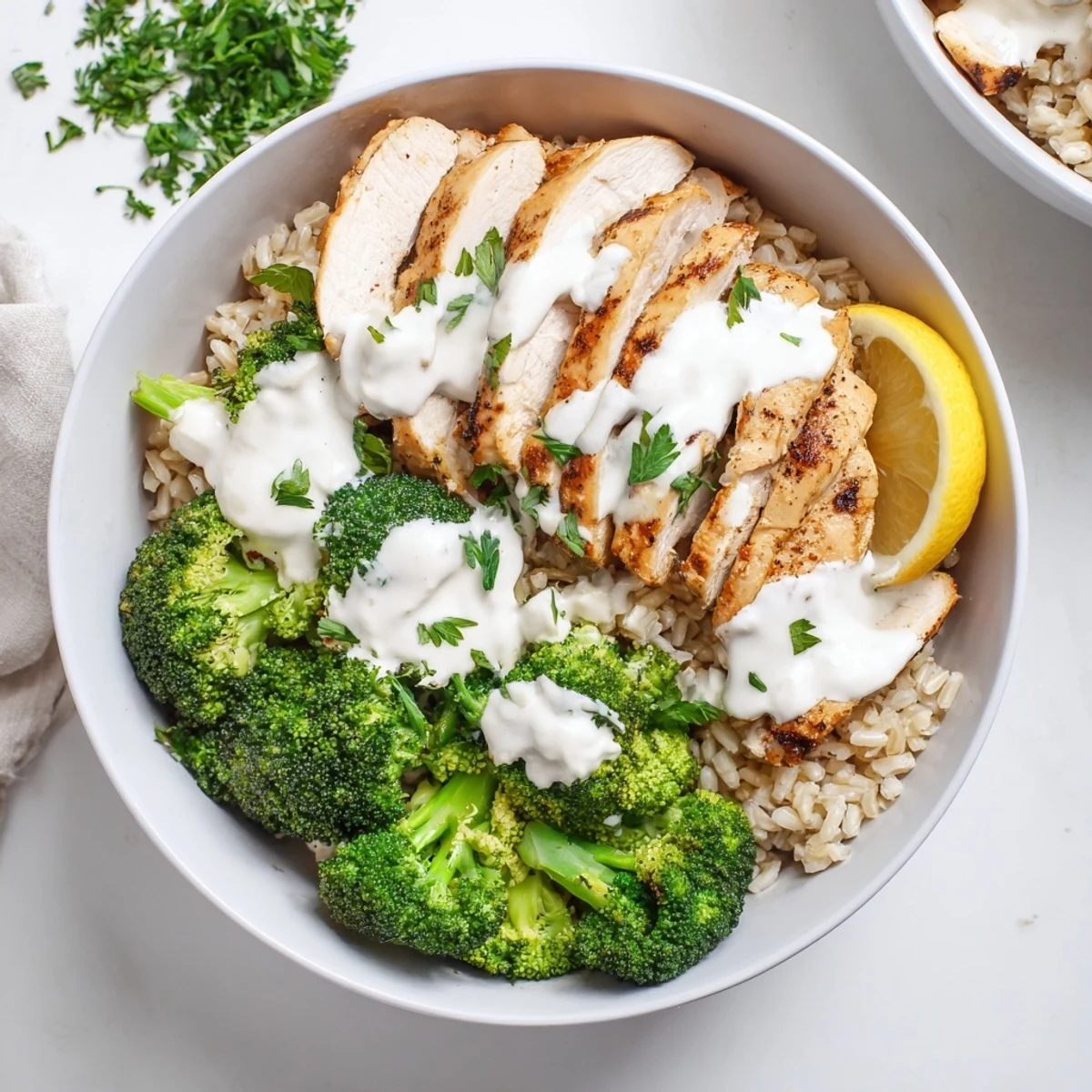 Healthy grilled chicken broccoli bowls drizzled with rich creamy garlic sauce over rice.