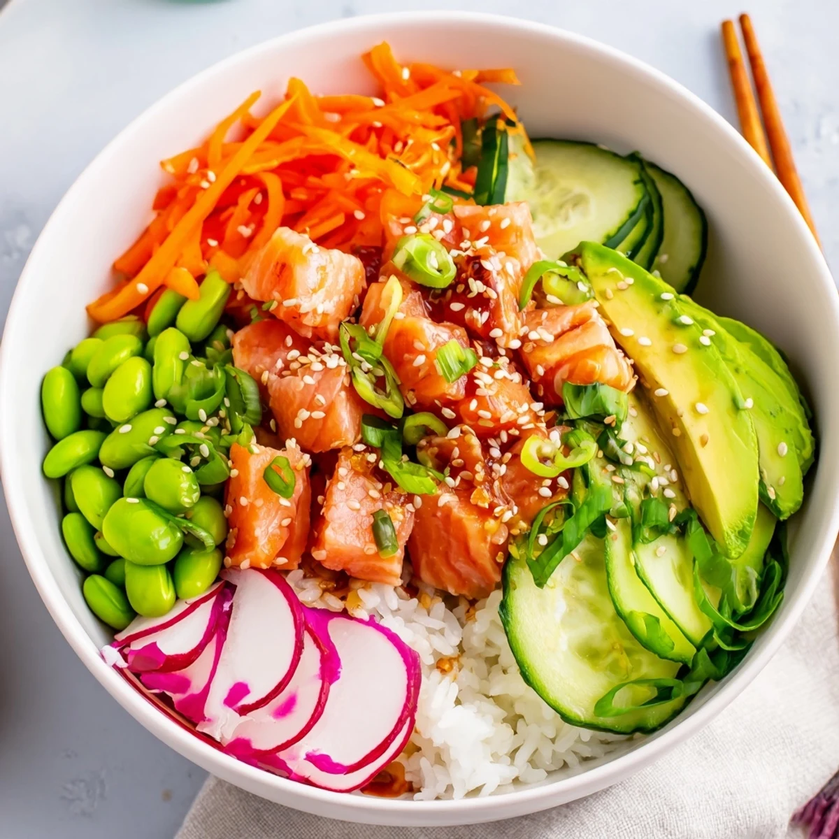 Homemade salmon poke bowl arranged with edamame, cucumber, and savory sesame sauce