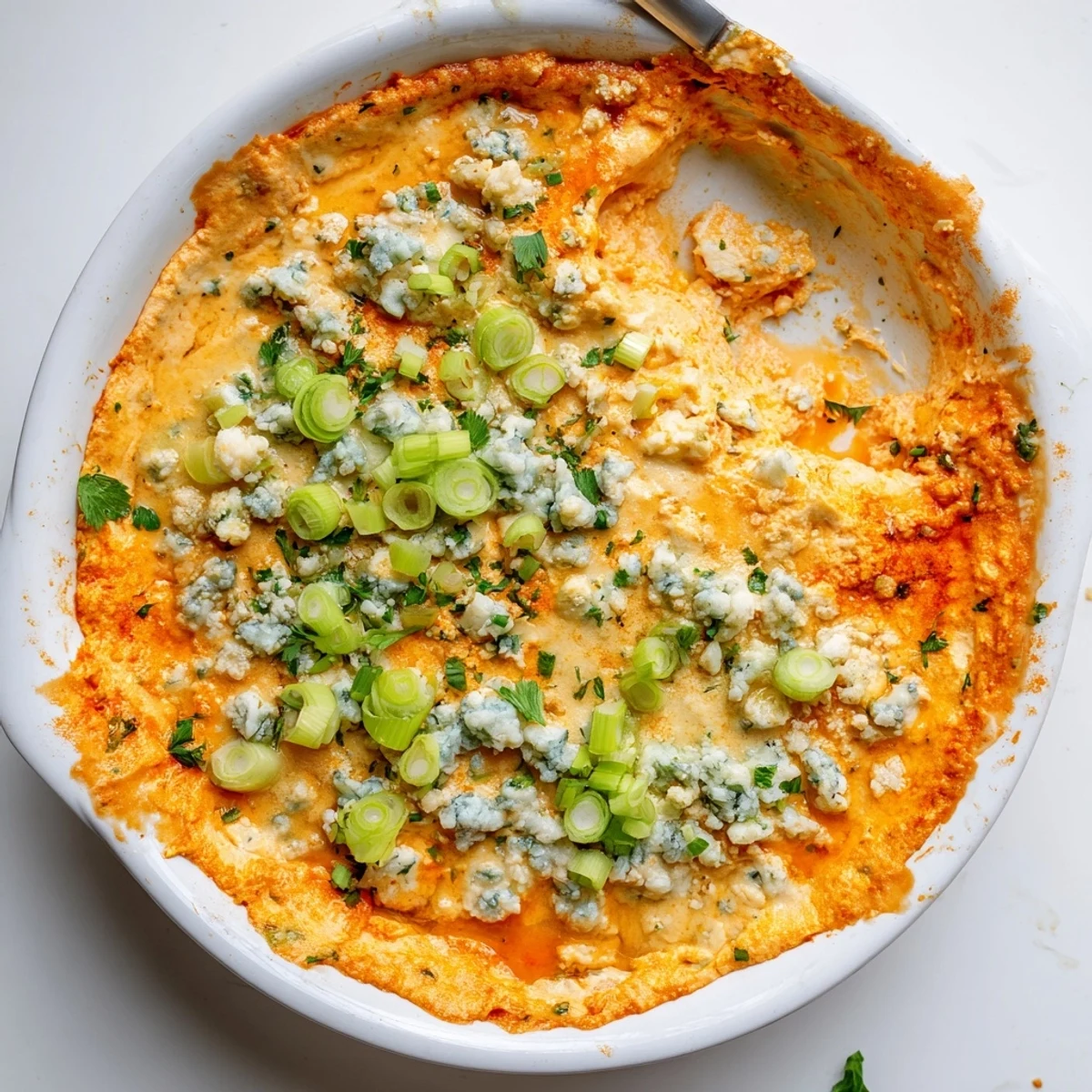 Golden baked cheesy white bean buffalo dip garnished with fresh green onions and parsley