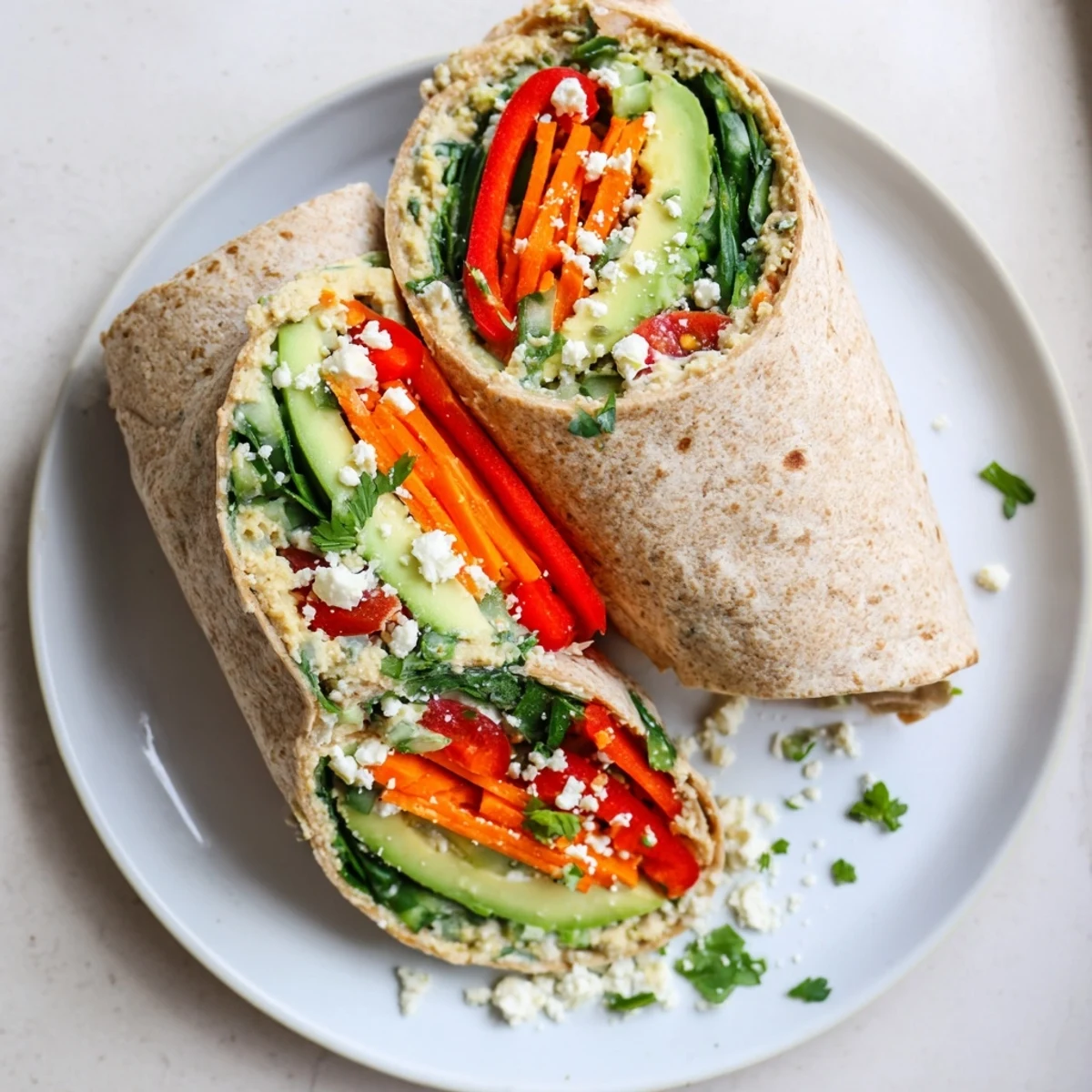 Healthy lunch featuring hummus veggie wrap rolled tight with spinach peppers and avocado