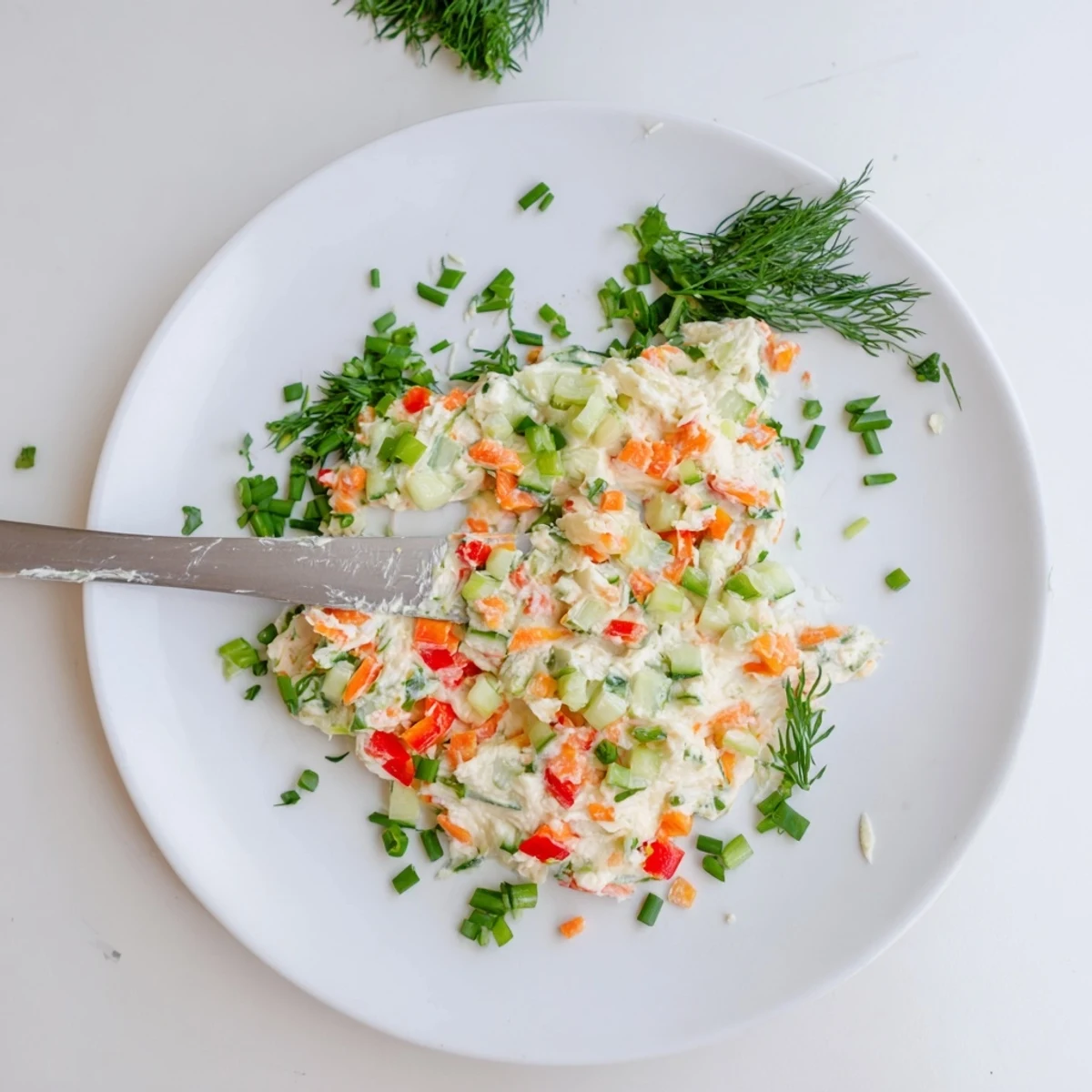 White bowl filled with garden vegetable spread featuring vibrant red bell pepper, cucumber, and green onions
