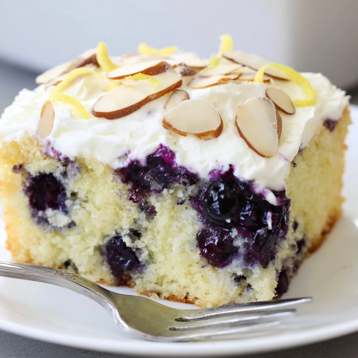 A bright Lemon Blueberry Poke Cake With Almond Topping served with tea, moist crumb.
