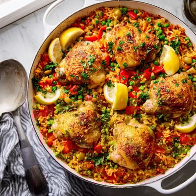 The finished One Pan Spanish Chicken and Rice Bake in a skillet, garnished with fresh parsley and served with lemon wedges for squeezing.