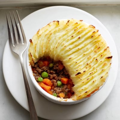 Mini Shepherds Pie with savory ground beef filling featuring carrots, peas, and onions in a ramekin.